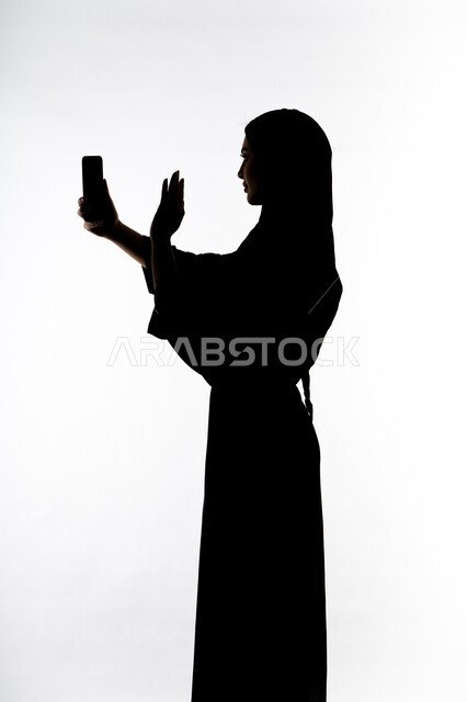 التقاط صور سيلفي تذكاريه بإستخدام الهاتف المحمول ،إستخدام اجهزة تقنية حديثة ، اجراء بث مباشر ،  اجراء مكالمه هاتفيه ،صورة ظلية لمرأة عربية خليجية اماراتيه ،وسائل التواصل الإجتماعي ، خلفية بيضاء