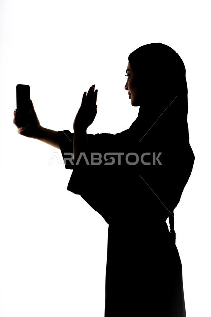 إستخدام اجهزة تقنية حديثة ، اجراء بث مباشر ، التقاط صور سيلفي تذكاريه بإستخدام الهاتف المحمول ، اجراء مكالمه هاتفيه ،صورة ظلية لمرأة عربية خليجية اماراتيه ،وسائل التواصل الإجتماعي ، خلفية بيضاء