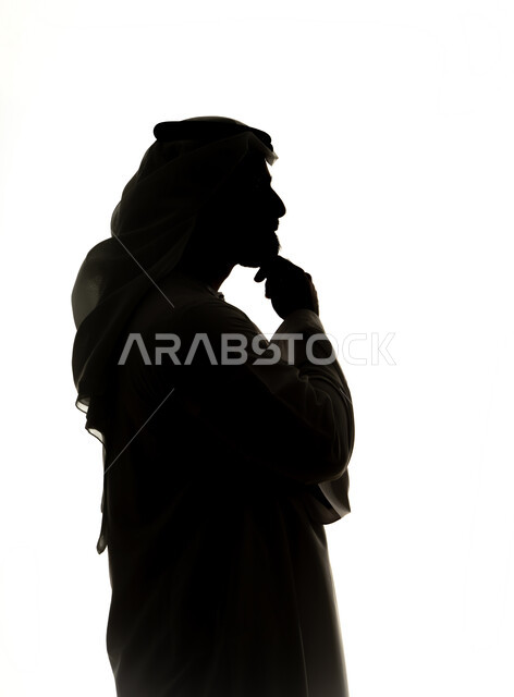 Finding a solution to a problem, contemplation and planning for the future, silhouette of an Emirati Gulf Arab man with his hand on his chin looking at a place with gestures of thinking and concentration, expressions of absent-mindedness and contemplation, white background