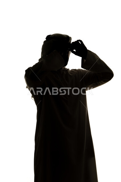 صورة ظلية لرجل عربي خليجي اماراتي يحمل بيده منظار ثنائي العينين و ينظر الى شيء ما ،إيماءات السرور والاستمتاع، رؤية الاشياء البعيدة و تقريبها,  حب الاستكشاف و المغامرة,  خلفية بيضاء