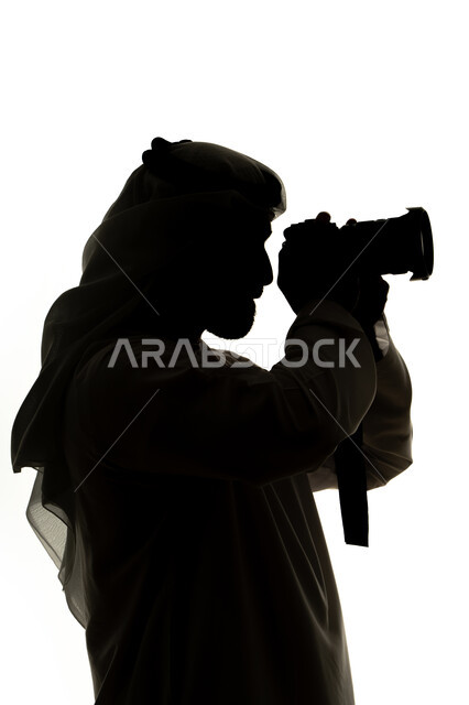 كاميرا عالية الدقة ، هواية التصوير ،صورة ظلية لرجل عربي خليجي اماراتي ، يحمل بيده كاميرا تصوير عالية الدقة ، إلتقاط الصور التذكارية ، مصوره اماراتي ، إحتراف التصوير ، خلفية بيضاء