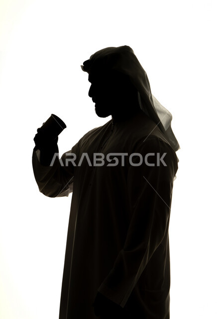 احتساء المشروبات الساخنة والأعشاب الشتوية الدافئة، تعديل المزاج بتناول الكافيين، صورة ظلية لرجل عربي خليجي اماراتي يحمل الفنجان ، مشروبات ساخنة ، خلفية بيضاء