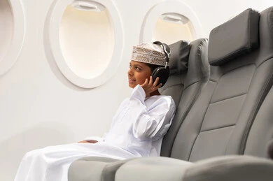 Entertainment and leisure using headphone technology, the concept of tourism and travel, preparing for an enjoyable summer vacation, an Omani Gulf Arab boy wearing a dishdasha and kumma sitting inside the airplane wearing headphones, listening to music through earphones.