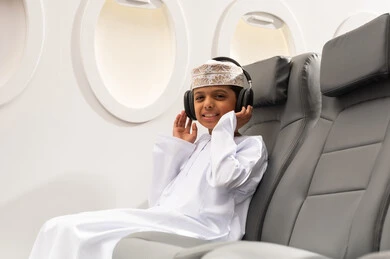 The concept of listening and hearing, the concept of tourism and travel, preparing to spend an enjoyable summer vacation, an Arab Gulf Omani boy wearing a dishdasha and a kumma, wearing headphones, listening to music through earphones.
