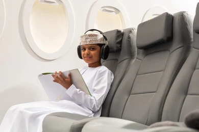 Enjoying a flight, creative artistic entertainment activities, a coloring game, an Arab Gulf Omani boy wearing a dishdasha and kumma and headphones sitting on a chair inside the airplane, Oman Air, the concept of tourism and travel.