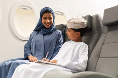 التعبير بالرسم عن الحب والمشاعر الإيجابية, مفهوم السياحة و السفر, التنقل باستخدام وسائل النقل الجوية, ولد عربية خليجي عماني يرتدي الدشداشة و الكمه يجلس على مقعده داخل الطائرة برفقه والدته يمسك كراسة التلوين و القلم , ايماءات السعادة و السرور