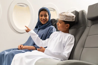 الاشارة الى شي ما, مفهوم السياحة و السفر, التنقل باستخدام وسائل النقل الجوية, ولد عربي خليجي عماني يرتدي الدشداشة و الكمة يجلس على مقعده داخل الطائرة برفقه والدته , ايماءات السعادة و السرور الاشارة الى شي ما, مفهوم السياحة و السفر, التنقل باستخدام وسائل النقل الجوية, ولد عربي خليجي عماني يرتدي الدشداشة و الكمة يجلس على مقعده داخل الطائرة برفقه والدته , ايماءات السعادة و السرور