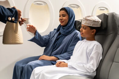 مفهوم السياحة و السفر, التنقل باستخدام وسائل النقل الجوية, الضيافة و حسن الاستقبال , امراة عربيه خليجيه عمانية ترتدي العباءة و الحجاب تجلس بجانب ابنها داخل الطائرة تقوم بشرب فنجان من القهوه