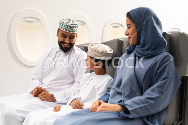 Spending the summer vacation with family, having a good time inside the airplane, an Omani Gulf Arab family wearing traditional attire sitting in their seats on a flight, gestures of happiness and joy, Oman Air.
