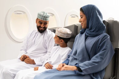 Spending the summer vacation with family, having a good time inside the airplane, an Omani Gulf Arab family wearing traditional attire sitting in their seats on a flight, gestures of happiness and joy, Oman Air.