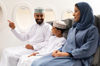 قضاء وقت ممتع داخل الطائرة , عائله عربيه خليجيه عمانية ترتدي الزي التقليدي تجلس على المقعد داخل الطائرة فى رحله جويه , ايماءات السعاده و السرور , رجل خليجي يقوم بالاشارة الى شيء ما