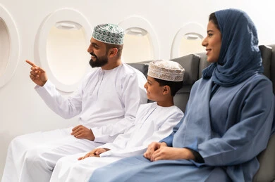 الانتقال عبر الطائرات الحديثة , الاستعداد لقضاء عطله صيفية ممتعه ,عائلة عربيه خليجيه عمانية ترتدي الزي التقليدي تجلس داخل الطائرة بايماءات السعاده و السرور , رجل عربي خليجي يرتدي الدشداشة و الكمه يقوم بالاشارة الي شيء ما