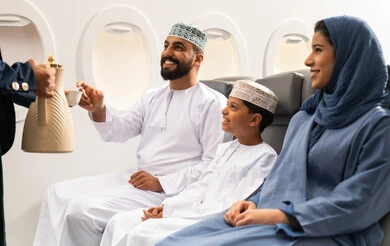 الإعتناء بالركاب ، حسن الضيافة والإستقبال ، عائلة عربيه خليجيه عمانية ترتدي الزي التقليدي تجلس داخل الطائرة , رجل عربي خليجي عماني يرتدي الدشداشة و الكمه يقوم بتناول كوب من القهوه , مفهوم السياحه و السفر, ايماءات السعاده و السرور