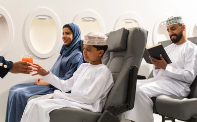 تقديم خدمات الطيران للركاب المسافرين, الإستقبال والترحيب بالركاب ، خطوط الطيران الجوي , الاستمتاع بتناول مشروبات , ولد عربي خليجي عماني يرتدي الدشداشة و الكمه برفقه عائلته يقوم بتناول كوب من العصير  داخل الطائرة, مفهوم السياحه و السفر