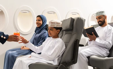الإستقبال والترحيب بالركاب ، خطوط الطيران الجوي ، تقديم خدمات الطيران للركاب المسافرين, الاستمتاع بتناول مشروبات , ولد عربي خليجي عماني يرتدي الدشداشة و الكمه برفقه عائلته يقوم بتناول كوب من العصير  داخل الطائرة, مفهوم السياحه و السفر