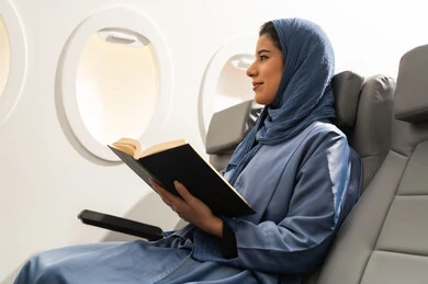 قضاء وقت الفراغ بالتعلم, الاستمتاع بقراءة الكتب والقصص والروايات, ثقافة التعلم الذاتي، ممارسة هواية المطالعة، امراة عربيه خليجيه عمانية ترتدي الحجاب و العباءة كرسي  داخل الطائرة فى رحله جويه تحمل بيدها كتاب و تنظر الى شيء ما