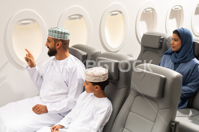 ايماءات تدل على الفرح والسعادة, الاشارة الى شيء ما, قضاء أوقات ممتعة داخل الطائرة ، عائلة مسافرة من العرب العمانيون الخليجيون داخل مقصورة الطائرة يرتدون الزي العماني، رحلات سياحية جويه ممتعة، عطلة صيفية عائلية، الخطوط الجوية العمانيه، سياحة وسفر