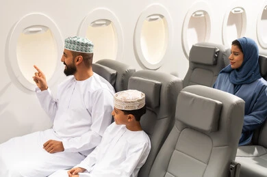 ايماءات تدل على الفرح والسعادة, الاشارة الى شيء ما, قضاء أوقات ممتعة داخل الطائرة ، عائلة مسافرة من العرب العمانيون الخليجيون داخل مقصورة الطائرة يرتدون الزي العماني، رحلات سياحية جويه ممتعة، عطلة صيفية عائلية، الخطوط الجوية العمانيه، سياحة وسفر