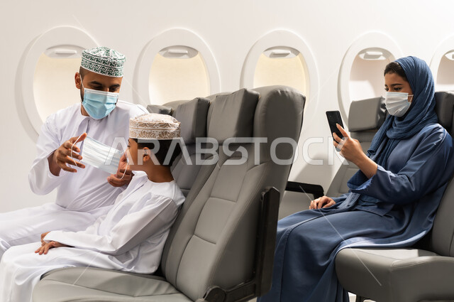 Following virus prevention measures, an Omani Gulf Arab family wearing traditional attire sits inside the airplane, wearing medical masks to protect against the coronavirus, airline companies, tourism and travel.