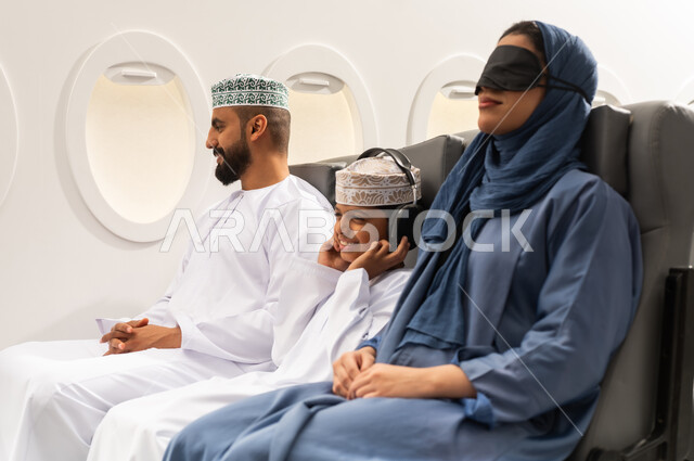 عائلة عربية خليجية عمانية ترتدي الزي التقليدي تجلس داخل الطائرة ، حسن الضيافة, السفر مع العائلة, خطوط الطيران الجوي ، سياحة وسفر ، امراة خليجيه ترتدي الماسك الاسود على عينها تنام على مقعدها , ايماءات السعادة و السرور