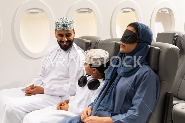 رحلة سياحية , خطوط الطيران الجوي, عائلة عربية خليجية عمانية ترتدي الزي التقليدي تجلس داخل الطائرة ، حسن الضيافة ، سياحة وسفر ، امراة خليجيه ترتدي الماسك الاسود على عينها تنام على مقعدها , ايماءات السعادة و السرور