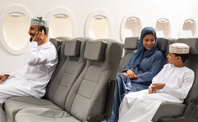 A Gulf man is making a phone call, having a good time, entertainment and fun while on the plane, an Arab Gulf Omani boy wearing a dishdasha and kumma sitting with his mother, preparing to spend an enjoyable summer vacation, gestures of happiness and joy.