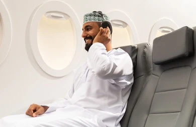 التفاعل والاندماج مع الأنغام الموسيقية, الاستماع للأغاني باسخدام الهيدفون، شاب عربي خليجي عماني يرتدي الدشداشة والكمه يجلس على كرسي الطائرة فى رحلة جوية يضع سماعات الرأس بإيماءات الفرح والسرور