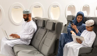 A Gulf man is working on a laptop, using modern technology in daily life. An Arab Gulf Omani family dressed in traditional attire is sitting inside an airplane on a flight. A Gulf mother is holding a mobile phone and pointing to something with her son, showing gestures of happiness and joy.