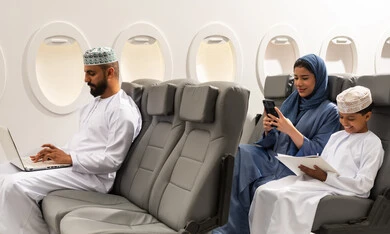 دمج التقنية والتكنولوجيا في الحياة العملية,عائله عربيه خليجيه عمانيه ترتدي الزي التقليدي تجلس داخل الطائرة فى رحله جويه , رجل خليجي يمسك بيده الحاسب المحمول , ام خليجيه تقوم بتصفح الهاتف المحمول بجانب ابنها , ايماءات السعادة و السرور