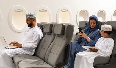 The concept of remote business management, entertainment, and leisure, tourism during the summer vacation, an Omani Gulf Arab family wearing traditional attire sitting inside an airplane on a flight, a Gulf man holding a laptop, a Gulf mother browsing her mobile phone next to her son, gestures of happiness and joy. The concept of remote business management, entertainment, and leisure, tourism during the summer vacation, an Omani Gulf Arab family wearing traditional attire sitting inside an airplane on a flight, a Gulf man holding a laptop, a Gulf mother browsing her mobile phone next to her son, gestures of happiness and joy.