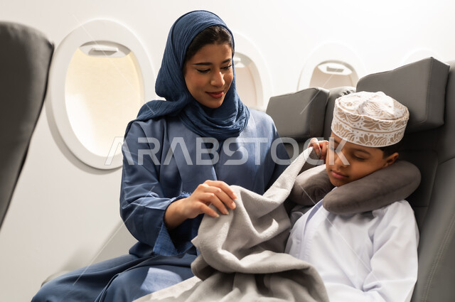 قضاء العطلة الصيفية في السفر والسياحه, عائله عربيه خليجيه عمانية ترتدي الزي التقليدي يجسلون على مقاعدهم فى رحله جوية , ام عربيه خليجيه تقوم بتغطية ابنها ,خطوط الطيران العماني