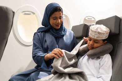 قضاء العطلة الصيفية في السفر والسياحه, عائله عربيه خليجيه عمانية ترتدي الزي التقليدي يجسلون على مقاعدهم فى رحله جوية , ام عربيه خليجيه تقوم بتغطية ابنها ,خطوط الطيران العماني