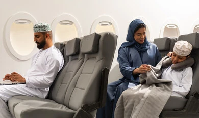 مفهوم اداره الاعمال والترفيه والتسليه عن بعد, عائله عربيه خليجيه عمانية ترتدي الزي التقليدي يجسلون على مقاعدهم فى رحله جوية , ام عربيه خليجيه تقوم بتغطية ابنها , رجل خليجي يمسك بيده الحاسب المحمول ، قضاء العطلة الصيفية في السفر والسياحه, خطوط الطيران العماني