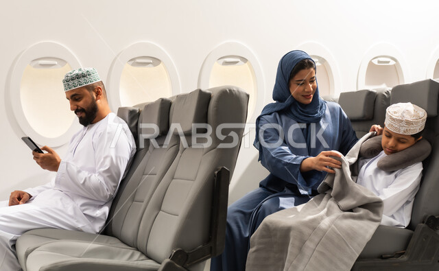 خطوط الطيران العماني, مفهوم النوم والراحه في الرحلة السياحية, عائله عربيه خليجيه عمانية ترتدي الزي التقليدي يجسلون على مقاعدهم فى رحله جوية , ام عربيه خليجيه تقوم بتغطية ابنها , رجل خليجي يمسك بيده الهاتف المحمول ، قضاء العطلة الصيفية في السفر والسياحه