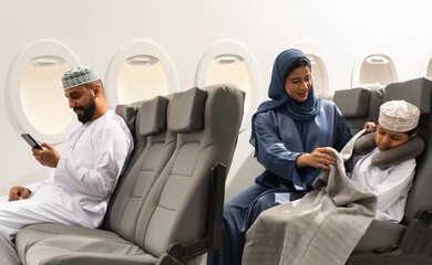 خطوط الطيران العماني, مفهوم النوم والراحه في الرحلة السياحية, عائله عربيه خليجيه عمانية ترتدي الزي التقليدي يجسلون على مقاعدهم فى رحله جوية , ام عربيه خليجيه تقوم بتغطية ابنها , رجل خليجي يمسك بيده الهاتف المحمول ، قضاء العطلة الصيفية في السفر والسياحه