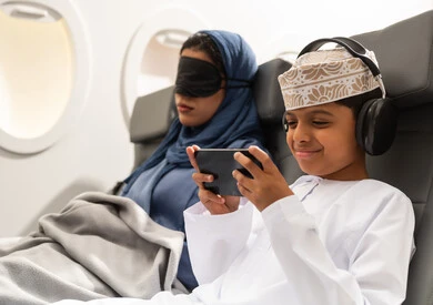 خطوط الطيران العماني, امراة عربيه خليجيه عمانية ترتدي العباءة و الحجاب تجلس على كرسي الطائرة فى رحله جويه تضع الماسك الاسود على عينها , ولد عربي خليجي يرتدي السماعات و يقوم بالعب على الهاتف المحمول بايماءات السعادة و السرور خطوط الطيران العماني, امراة عربيه خليجيه عمانية ترتدي العباءة و الحجاب تجلس على كرسي الطائرة فى رحله جويه تضع الماسك الاسود على عينها , ولد عربي خليجي يرتدي السماعات و يقوم بالعب على الهاتف المحمول بايماءات السعادة و السرور