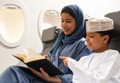 Spending the summer vacation with family, a family sightseeing trip, a boy spending the trip with his mother pointing at something, an Arab Gulf Omani woman wearing an abaya and hijab holding a book in her hands, Oman Air, gestures of happiness and joy.