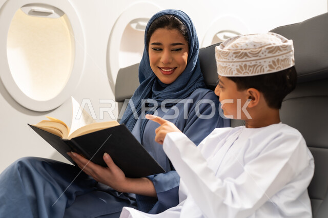 رحلة سياحية عائلية، ولد يقضي وقت الرحلة برفقة والدته يقوم بالاشارة الى شي ما، امرأة عربية خليجية عمانية ترتدي العباءة و الحجاب تمسك بيديها كتاب، قضاء العطلة الصيفية برفقة العائلة، خطوط الطيران العماني, ايماءات السعادة و السرور