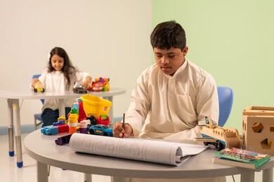 ولد عماني مصاب بمتلازمه داون يقوم بالرسم والتلوين ، تنمية المهارات الفنيه في الروضات السعودية  ،بنت عربيه سعوديه ترتدي الزي الكاجوال تجلس على كرسي متحرك، تلعب بالالعاب البلاستيكيه الملونه، مفهوم الاهتمام بالهوايات،قضاء اوقات ممتعه