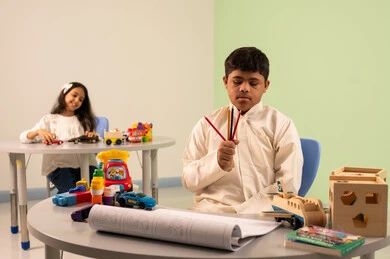 مفهوم الاهتمام بالهوايات،تنمية المهارات الفنيه في الروضات السعودية  ،ولد عماني مصاب بمتلازمه داون ينظر الى الكاميرا بايماءات السعاده،بنت عربيه سعوديه ترتدي الزي الكاجوال تجلس على كرسي متحرك، تلعب بالالعاب البلاستيكيه الملونه، قضاء اوقات ممتعه