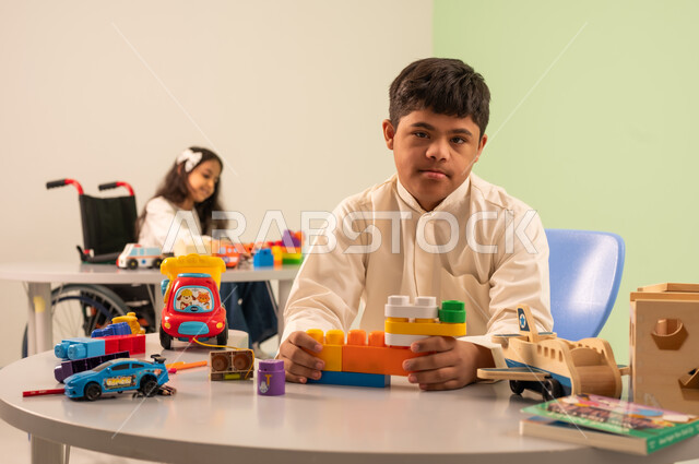 Recreational activities for people with special needs, Saudi society's interest in people of determination, having fun, creativity and developing mental and intellectual skills in Saudi kindergartens, encouraging, caring for and developing children's skills, a Saudi Arabian boy with Down syndrome assembling blocks with happy expressions