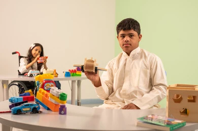 تشجيع ورعاية وتطوير مهارات الأطفال،  اهتمام المجتمع السعودي بأصحاب الهمم,  الابداع وتنمية المهارات الذهنيه والفكريه في الروضات السعودية ، بنت عربيه سعوديه ترتدي الزي الكاجوال تجلس على كرسي متحرك، تقوم بتركيب المكعبات بتعابير السعاده ،نشاطات ترفيهية لذوي الاحتياجات الخاصة ،ولد عماني مصاب بمتلازمه داون يقوم باللعب بالالعاب البلاستيكيه الملونه