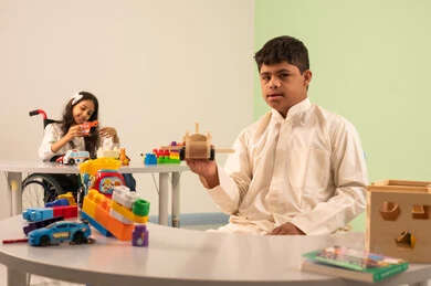 الابداع وتنمية المهارات الذهنيه والفكريه في الروضات السعودية ، تشجيع ورعاية وتطوير مهارات الأطفال،  اهتمام المجتمع السعودي بأصحاب الهمم, بنت عربيه سعوديه ترتدي الزي الكاجوال تجلس على كرسي متحرك، تقوم بتركيب المكعبات بتعابير السعاده ،نشاطات ترفيهية لذوي الاحتياجات الخاصة ،ولد عماني مصاب بمتلازمه داون يقوم باللعب بالالعاب البلاستيكيه الملونه