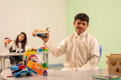 نشاطات ترفيهية لذوي الاحتياجات الخاصة ،الابداع وتنمية المهارات الذهنيه والفكريه في الروضات السعودية ، تشجيع ورعاية وتطوير مهارات الأطفال،  اهتمام المجتمع السعودي بأصحاب الهمم, بنت عربيه سعوديه ترتدي الزي الكاجوال تجلس على كرسي متحرك، تقوم بتركيب المكعبات بتعابير السعاده ،ولد عماني مصاب بمتلازمه داون يقوم باللعب بالالعاب البلاستيكيه الملونه