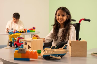 تشجيع ورعاية وتطوير مهارات الأطفال، اهتمام المجتمع السعودي بأصحاب الهمم, نشاطات ترفيهية لذوي الاحتياجات الخاصة ، الابداع وتنمية المهارات الذهنيه والفكريه في الروضات السعودية ، بنت عربيه سعوديه ترتدي الزي الكاجوال تجلس على كرسي متحرك، تقوم باللعب بالالعاب الخشبيه بتعابير السعاده ،  ولد عماني مصاب بمتلازمه داون يقوم باللعب بالالعاب البلاستيكيه الملونه