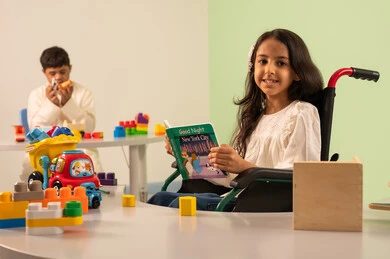 تعزيز النشاط الذهني ، قضاء اوقات ممتعه ، تنمية المهارات الذهنيه والفكريه في الروضات السعودية ، مفهوم هوايه المطالعه ، بنت عربيه سعوديه ترتدي الزي الكاجوال تجلس على كرسي متحرك، تقوم بقراءه الكتب التعليميه الملونه بتعابير السعاده ، ولد عماني مصاب بمتلازمه داون يقوم بتركيب المكعبات