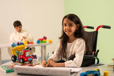 Looking at the camera with gestures of joy, developing artistic skills in Saudi kindergartens, expressions of focus and enjoyment, the concept of interest in hobbies, spending enjoyable times, a Saudi boy with Down syndrome playing with blocks, an Omani Arab girl wearing casual clothes drawing and coloring