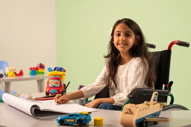 Developing artistic skills in Saudi kindergartens, having fun, the concept of caring for hobbies, a Saudi Arabian girl wearing casual clothes sitting in a wheelchair, drawing and coloring with expressions of concentration and enjoyment