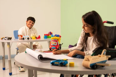 مفهوم الاهتمام بالهوايات،ولد عماني مصاب بمتلازمه داون ينظر الى الكاميرا بايماءات السعاده،تنمية المهارات الفنيه في الروضات السعودية ،  قضاء اوقات ممتعه ، بنت عربيه سعوديه ترتدي الزي الكاجوال تجلس على كرسي متحرك، تقوم بالرسم والتلوين بتعابير التركيز والاستمتاع