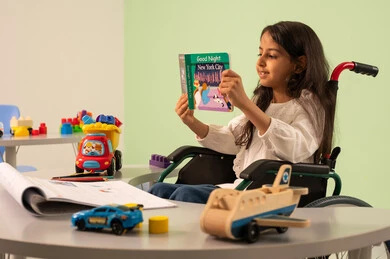 مفهوم هوايه المطالعه ، تعزيز النشاط الذهني ،  تنمية المهارات الذهنيه والفكريه في الروضات السعودية ،  قضاء اوقات ممتعه ، بنت عربيه سعوديه ترتدي الزي الكاجوال تجلس على كرسي متحرك، تقوم بقراءه الكتب التعليميه الملونه بتعابير السعاده